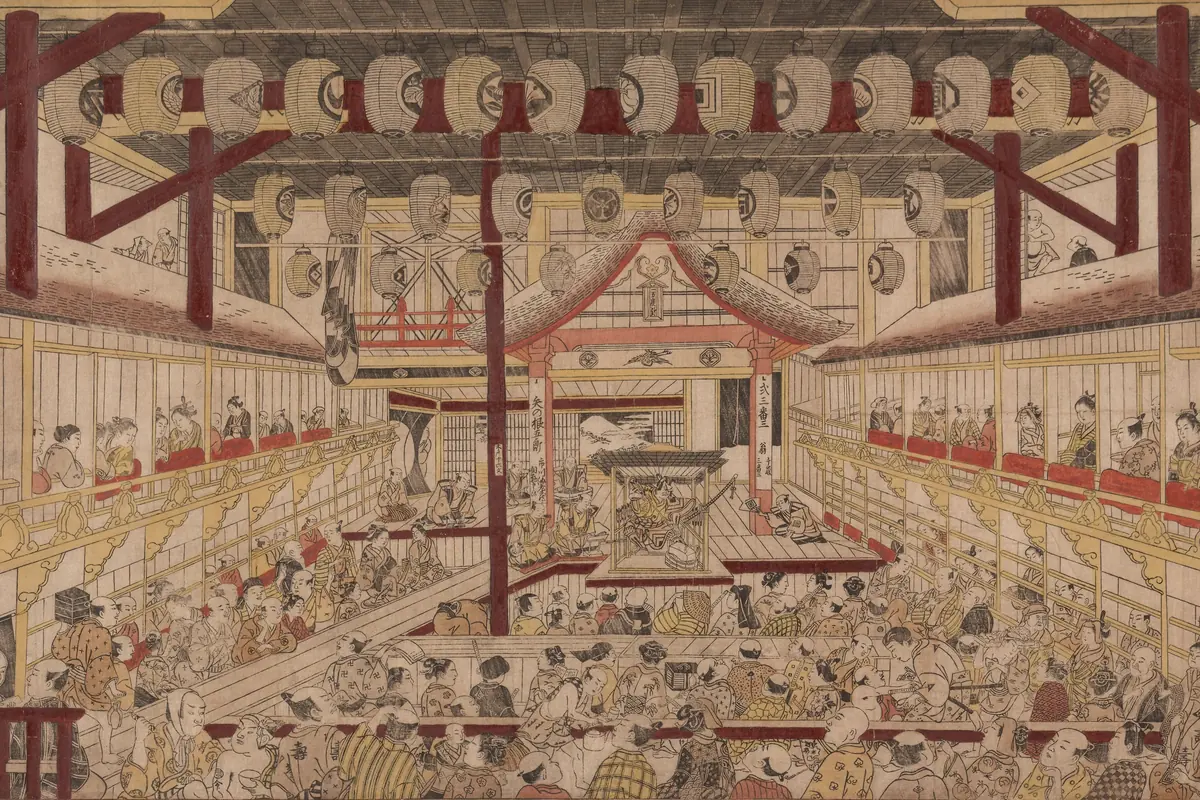A colour print looking down the length of a crowded Edo theatre toward a raised stage, with boxes along both sides and paper lanterns hung overhead