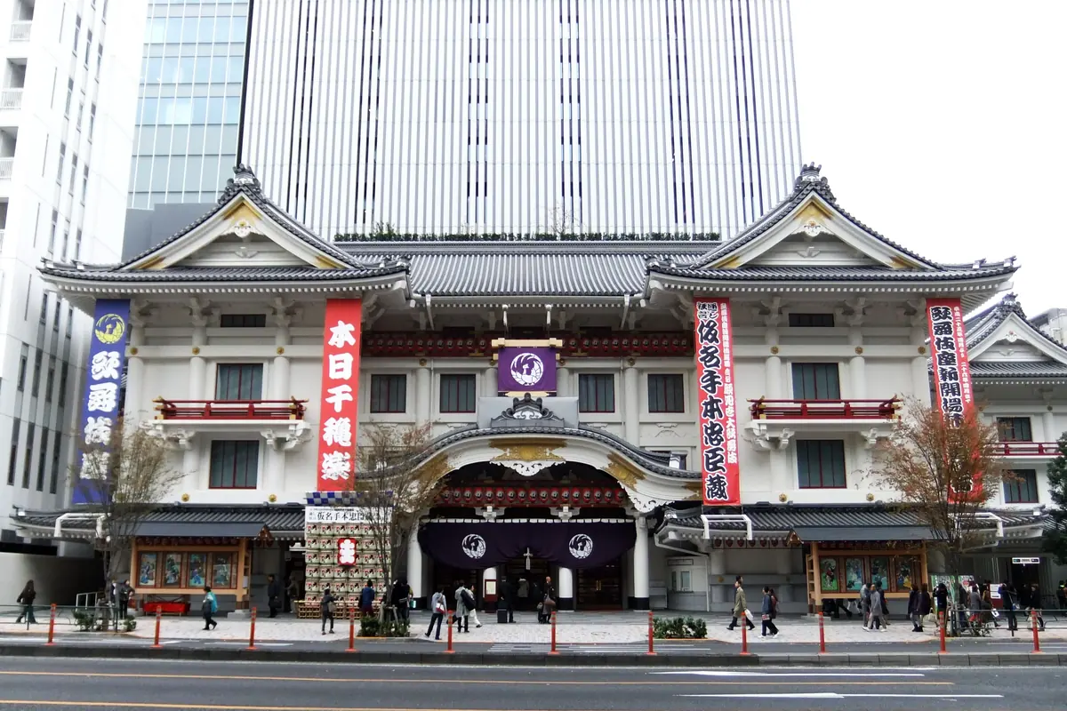 The white and red front of the Kabuki-za theatre in Ginza, with a tall office tower rising behind it and pedestrians along the pavement