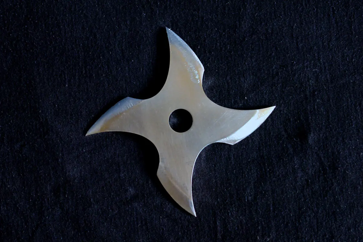A four-pointed steel throwing star with a round centre hole lying on a dark cloth